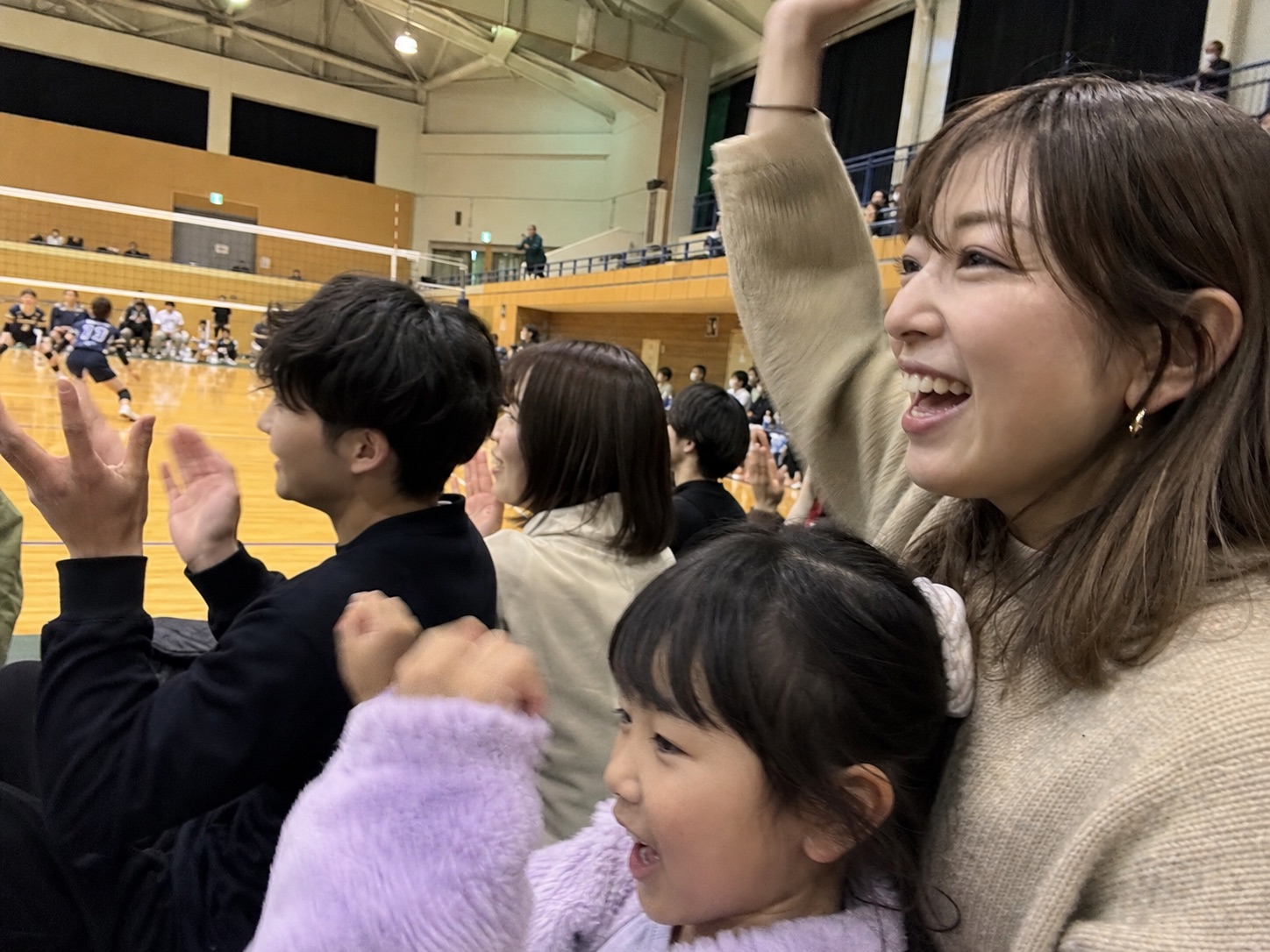 市立体育館でバレーボールを応援する親子と来場者
